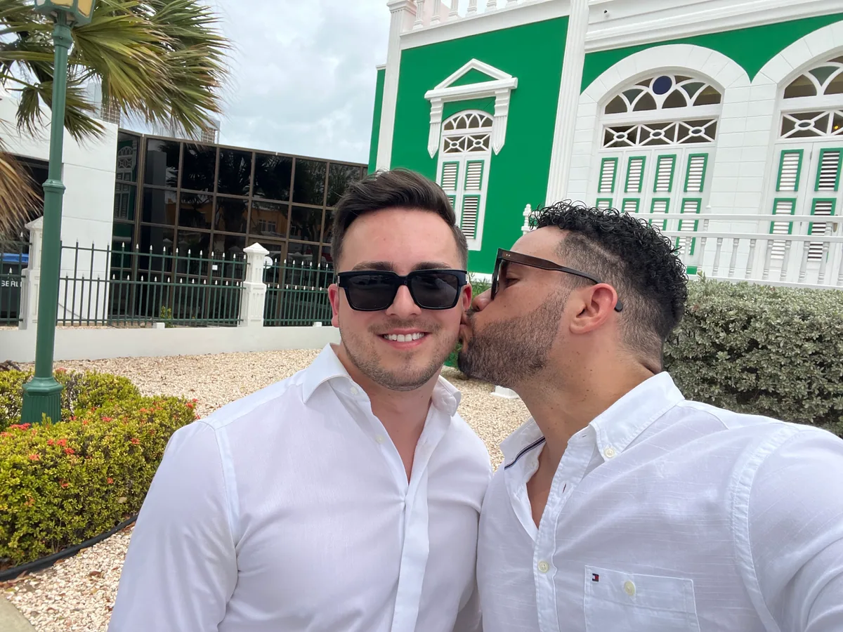 Derick kissing Klaudio outside a green historic building